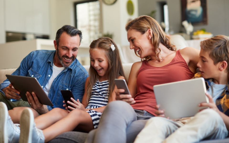 Fröhliche Familie mit digitalen Endgeräten auf Sofa